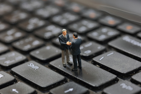 Selective focus of miniature business man handshake on the button Enter button keyboard of laptop as commitment and partnership concept.の写真素材