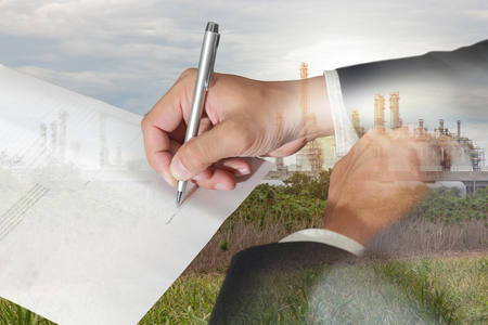 Double exposure of businessman hand holding a pen signing to the document, electric generating plant and sunset in the evening as Energy and Business concept.の写真素材