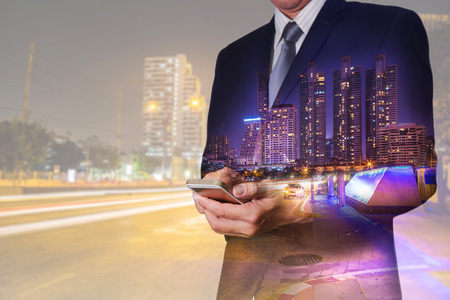 Double exposure of business man hand hold smart phone, mobile , city, urban and street at night as business, telecommunication, technology and communication concept.の写真素材