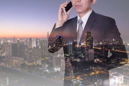 Double exposure of businessman calling with smartphone and  night cityscape as technology and telecommunication concept.の写真素材
