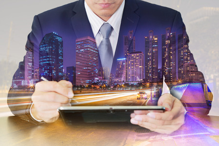 Double exposure of businessman working with tablet urban, city and street at night as business, technology and communication concept.の写真素材