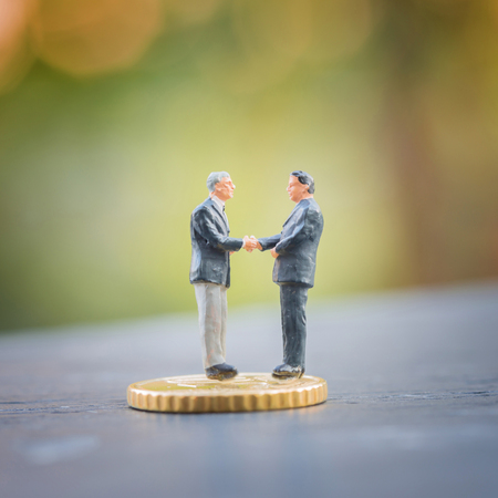 Selective focus of miniature businessman handshake on Euro coins as business , commitment, investment, teamwork and partnership conceptの写真素材