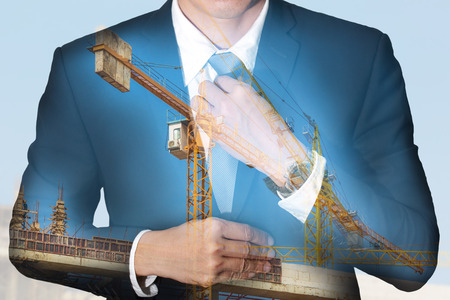Businessman held necktie dress to look good, construction crane and building under blue sky as business, industrial and vision of leader conceptの写真素材