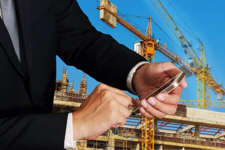 Businessman use smartphone on blur crane construction and building background as Technology, telecommunication and Communication concept.の写真素材