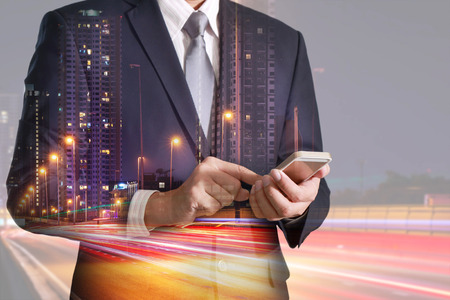 Double exposure of businessman hand hold and touch screen smartphone, mobile, light trails on the street and urban in the night as business, technology, telecommunication and communication concept.の写真素材