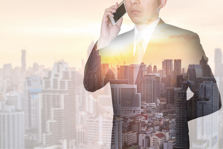 Double exposure of businessman calling with smartphone, cityscape, urban and sunset as business, technology and telecommunication concept.の写真素材