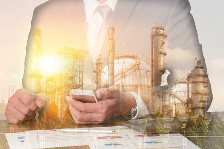Double exposure of businessman working with smartphone, oil fuel, Electric generating factory or plant with sunset as business, technology, communication, industrial and energy concept.の写真素材