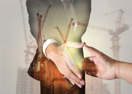 Double exposure of businessman will handshaking for business relationship, construction crane, building and sunlight of sunset as business, industry, commitment and partnership concept.の写真素材