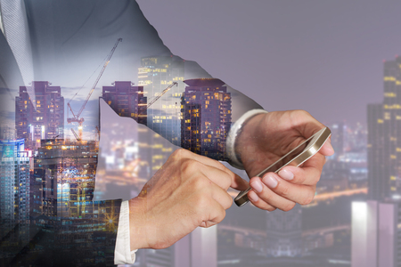 Double exposure of businessman use smartphone, construction crane, buildilng, urban and city in the night as business, industry, technology, telecommunication and Communication concept.の写真素材