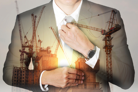 Double exposure of businessman held necktie dress to look good, construction crane, bulilding and sunlight of sunset as business and industrial concept.の写真素材