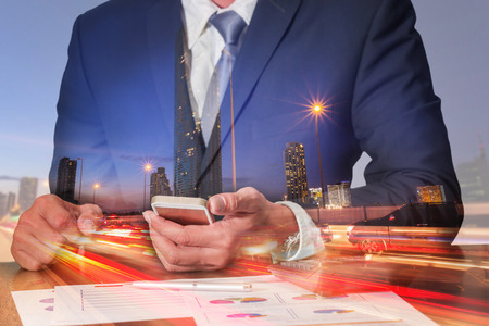 Double exposure of businessman working with smartphone light trails on the street and urban at dusk, night as commitment, technology and communication concept.の写真素材