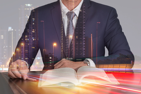 Double exposure of businessman sitting at meeting room to open the book, light trails on the street and urban in the night as business and Learning concept.の写真素材