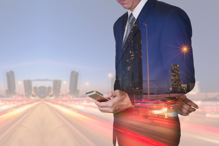 Double exposure of businessman stand up and research by smartphone, light trails on the street and urban at dusk, night as technology and business concept.の写真素材