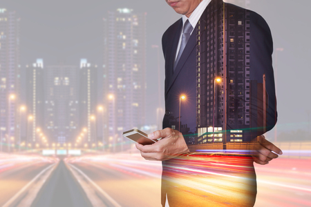 Double exposure of businessman stand up and research by smartphone, light trails on the street and urban in the night as technology, telecommunication and business concept.の写真素材