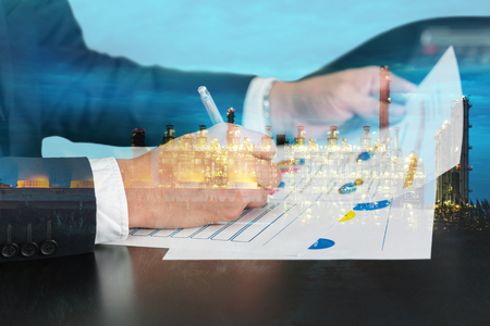Double exposure of businessman hand hold a pen write, review document and electric generating factory industry in the twilight or night as energy, business, review and working Concept.の写真素材