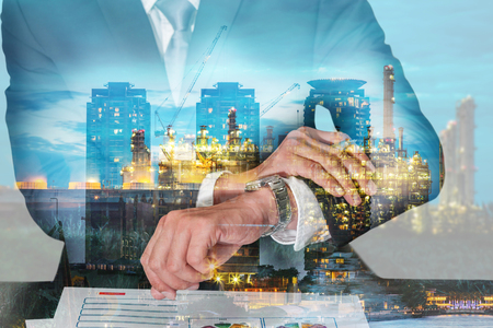 Double exposure of businessman look the watch, construction crane and electric generating factory industry in the twilight or night as appointment and business concept.の写真素材