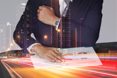 Businessman hand put on the chart document, light trails on the street and urban in the night as business, meeting and analysis concept.の写真素材