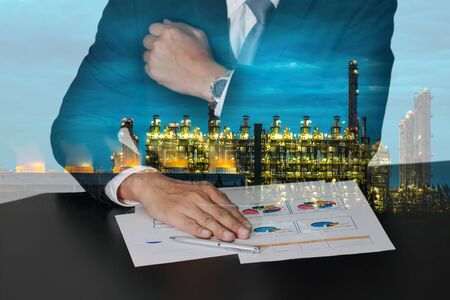 Businessman hand put on the chart document and electric generating factory industry in the twilight or night as energy, business, meeting and analysis concept.の写真素材