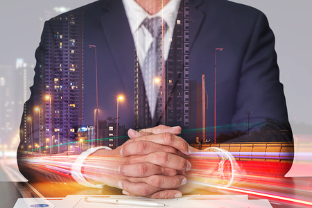Double exposure of businessman fingers crossed and sit down, light trails on the street and urban at dusk, night as meeting, commitment and business concept.の写真素材