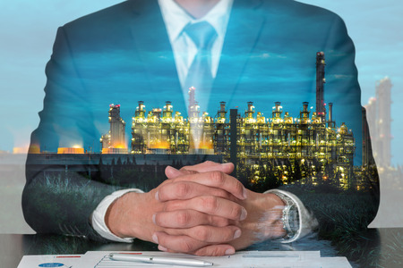 Double exposure of businessman fingers crossed and sit down, Electric generating factory industry at night as energy, meeting, commitment and business concept.の写真素材