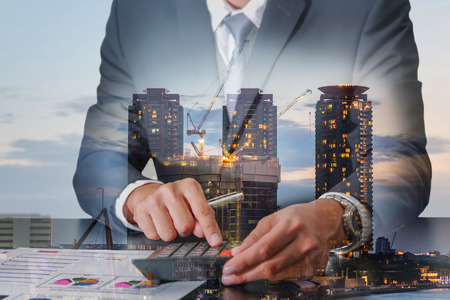 Double exposure of businessman working with calculator and construction crane and building in the evening, twilight as Worker, Commitment, Calculation and industrial conceptの写真素材