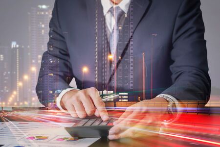 Double exposure of businessman working with calculator and light trails on the street and urban in the night as Worker, Commitment and Calculation conceptの写真素材
