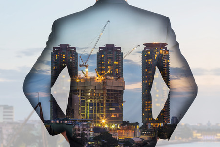 A back turned businessman and construction crane and building in the evening, twilight as business, vision of leader and industrial conceptの写真素材