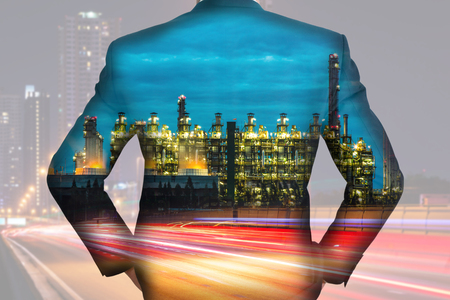 A back turned businessman, light trails on the street and urban, Electric generating factory industry in the night as energy, business and vision of leader conceptの写真素材