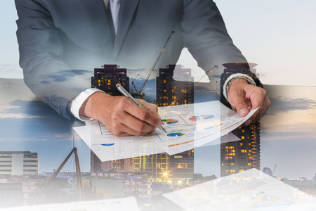 Double exposure of businessman review charts, construction crane and building in the evening, twilight as business, analysis and industrial concept.の写真素材