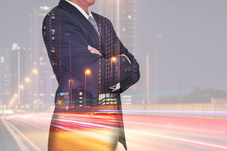 Double exposure of Businessman arms crossed and stand up and light trails on the street and urban in the night as thinking vision of leader concept.の写真素材