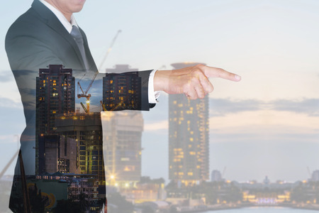 Double exposure of businessman finger point virtual target, construction crane and building in the evening, twilight as business, target and industrial concept.の写真素材