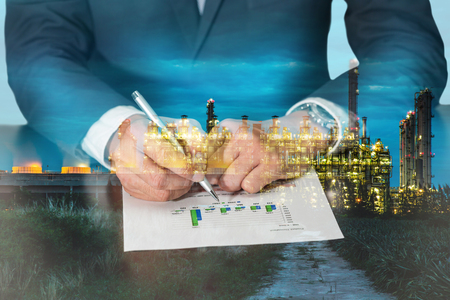 Double exposure of businessman hand hold a pen point to the bar graph, electric generating factory industry in the twilight or night as Business, commitment, analysis and energy conceptの写真素材