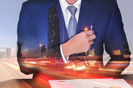Double exposure of businessman holding a pen on the pocket, light trails on the street and urban at dusk, night as business and analysis conceptの写真素材