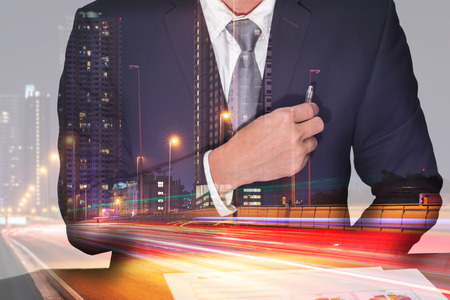 Double exposure of businessman holding a pen on the pocket, light trails on the street and urban in the night as business and analysis conceptの写真素材