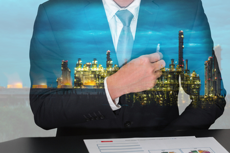 Double exposure of businessman holding a pen on the pocket, electric generating factory industry in the twilight or night as energy, business and analysis concept.の写真素材