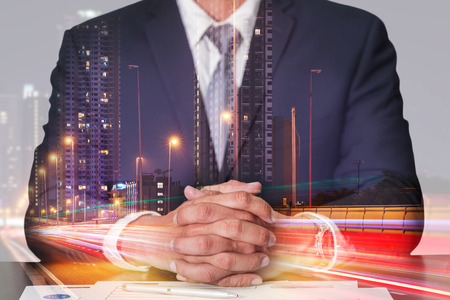 Double exposure of businessman fingers crossed and sit down, light trails on the street and urban at dusk, night as meeting, commitment and business concept.の写真素材