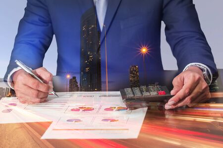 Double exposure of businessman working with document and calculator for analyze in the work, light trails on the street and urban at dusk, night as analysis and commitment concept.の写真素材