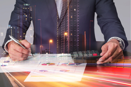 Double exposure of businessman working with document and calculator for analyze in the work light trails on the street and urban in the night as, business, analysis and commitment concept.の写真素材