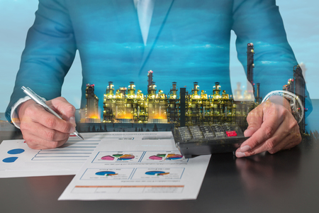 Double exposure of businessman working with document and calculator for analyze in the work and electric generating factory industry in the night as energy, business, analysis and commitment concept.の写真素材