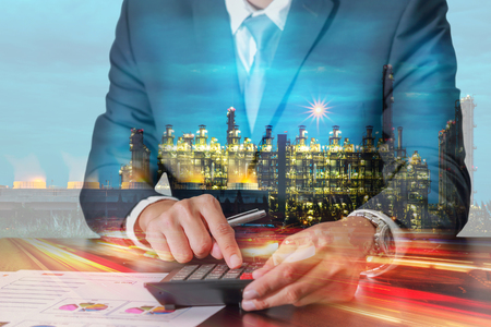 Double exposure of businessman working with calculator, light trails street urban and electric generating factory industry in the night as business, energy, worker, commitment and calculation conceptの写真素材