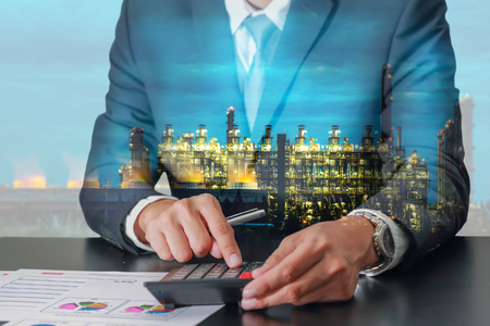 Double exposure of businessman working with calculator and Electric generating factory industry in the night as business, energy, worker, commitment and calculation conceptの写真素材