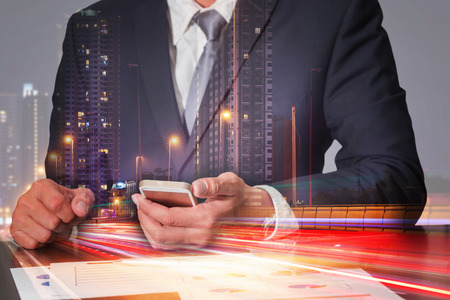 Double exposure of businessman working with smartphone light trails on the street and urban in the night as commitment, technology and communication concept.の写真素材
