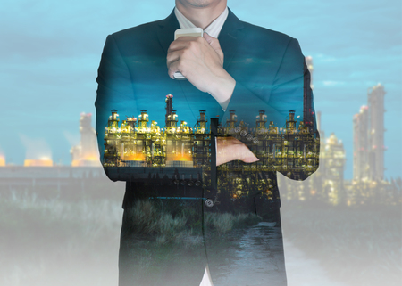 Double exposure of businessman stand up and think idea about business, electric generating factory industry in the night as business, energy and thoughtful concept.の写真素材