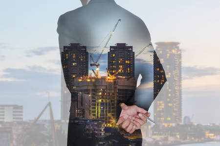 Double exposure of businessman think and analyze the work, construction crane and building in the evening, twilight as business, vision of leader and industrial conceptの写真素材