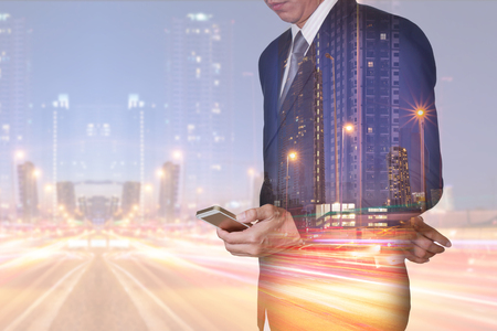 Double exposure of businessman stand up and research by smartphone, light trails on the street and urban at dusk, night as technology, communication and business concept.の写真素材