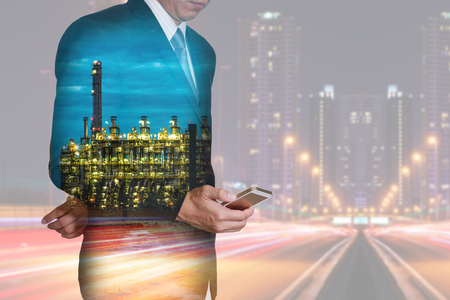 Double exposure of businessman stand up and research by smartphone, Electric generating factory industry and light trails on night street as business technology, telecommunication and energy concept.の写真素材