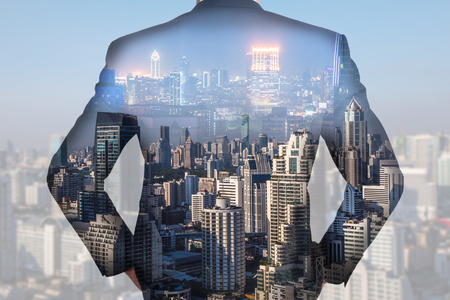 Double exposure of A back turned businessman and cityscape,urban in the night and the day as business and vision of leader concept.の写真素材
