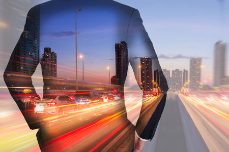 Double exposure of businessman Back, looking ahead, light trails on the street and urban in the twilight, night as business, leadership, goal and success conceptの写真素材