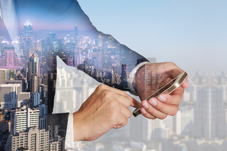 Double exposure of businessman use smartphone, cityscape, urban in the night and the day as business, Technology, telecommunication and Communication concept.の写真素材