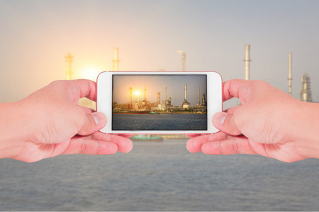 hand hold smartphone, cellphone to take a photo, oil fuel, Electric generating factory, plant near the river and sunset as industry, energy, communication and technology concept.の写真素材